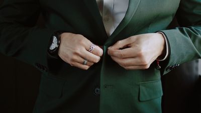 Groom buttons his emerald green tuxedo jacket, detail of watch and ring