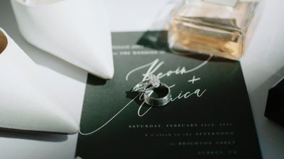 Wedding rings resting on a black calligraphy invitation in soft light